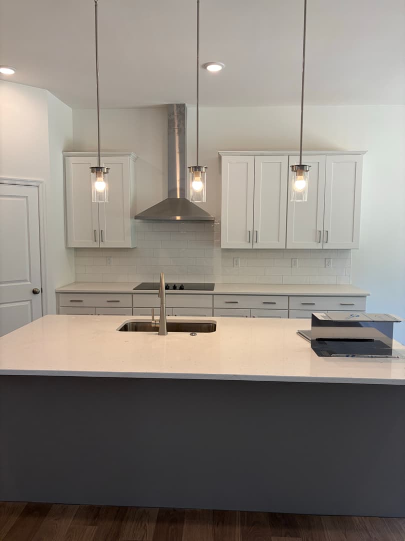 Finished kitchen with white cabinets, quartz island, and pendant lights
